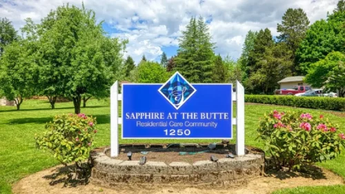 A large blue sign for _Sapphire at the Butte Residential Care Community_ on a stone base, set in a grassy area with trees